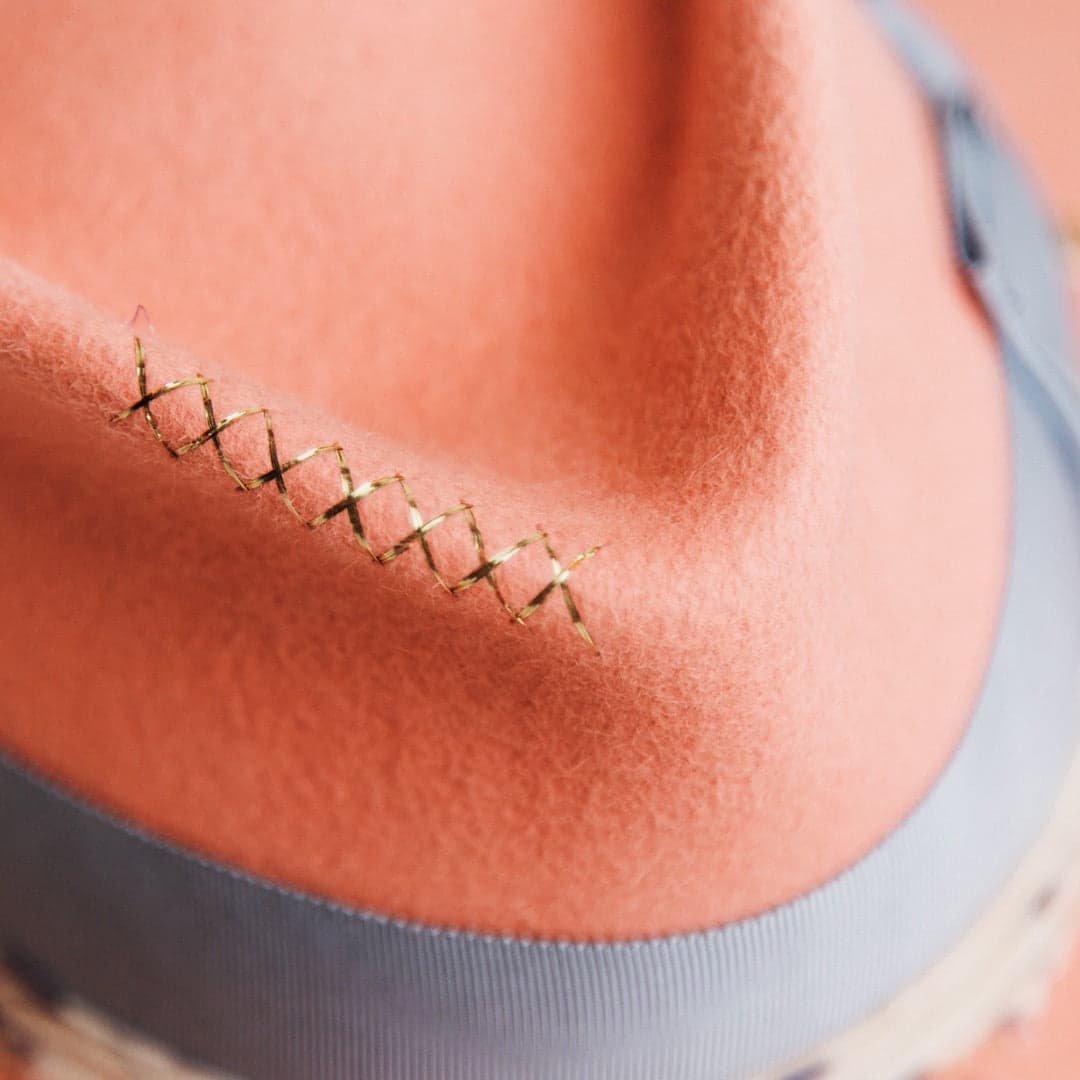 Close up detail of the Pāua felt hat showing metallic gold hand-stitched cross detailing on the peach rabbit felt crown.