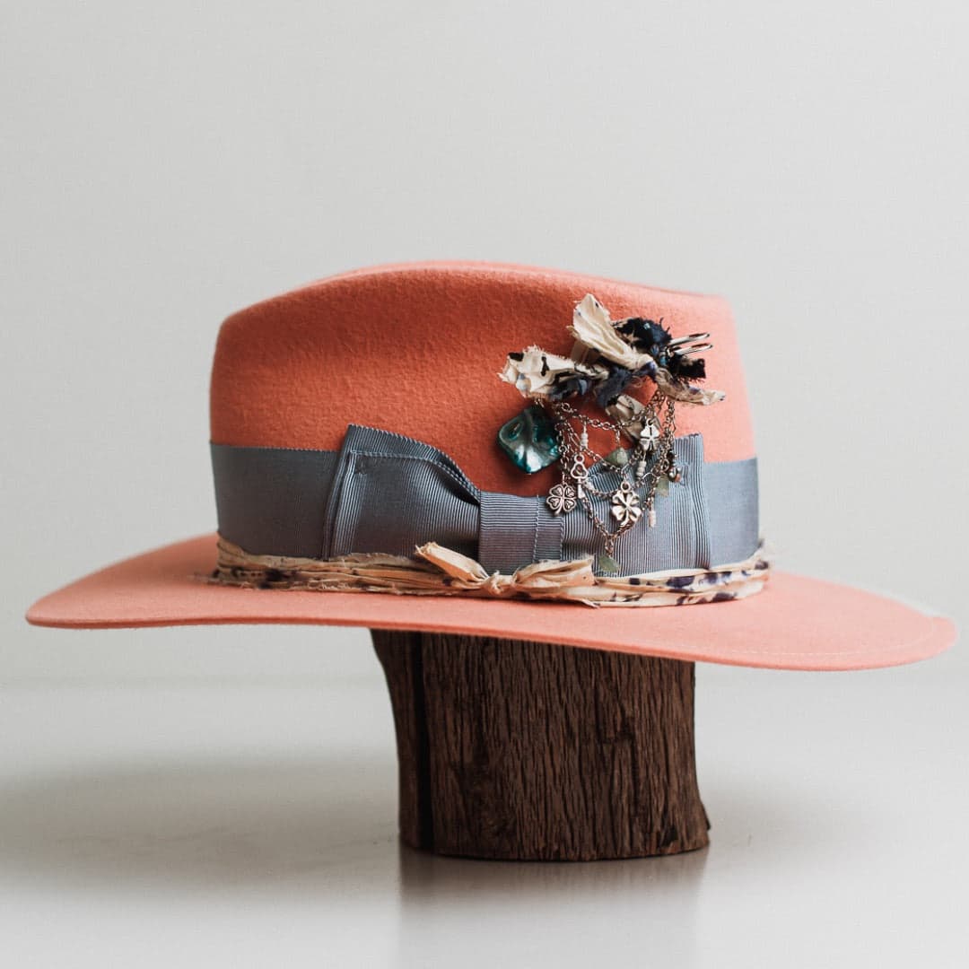 Left side view of the Pāua peach felt hat by PHYLLi Designs with ivory 1/3 brim trim and speckled cream and blue sari silk trimming.