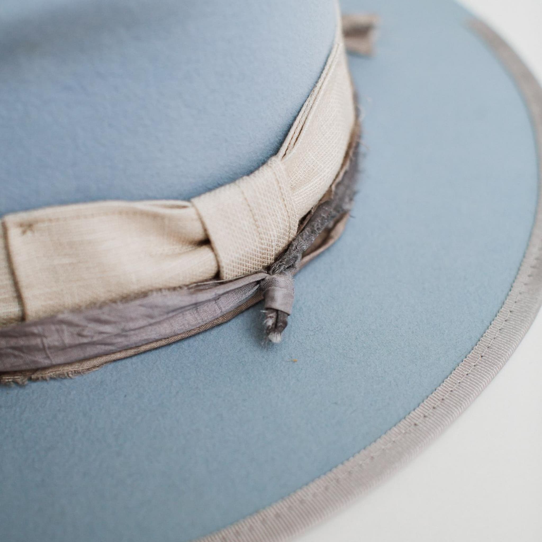 Close-up detail of Perfect Storm crystal blue felt hat by PHYLLi Designs showing hand-stitched crosses and natural linen band.