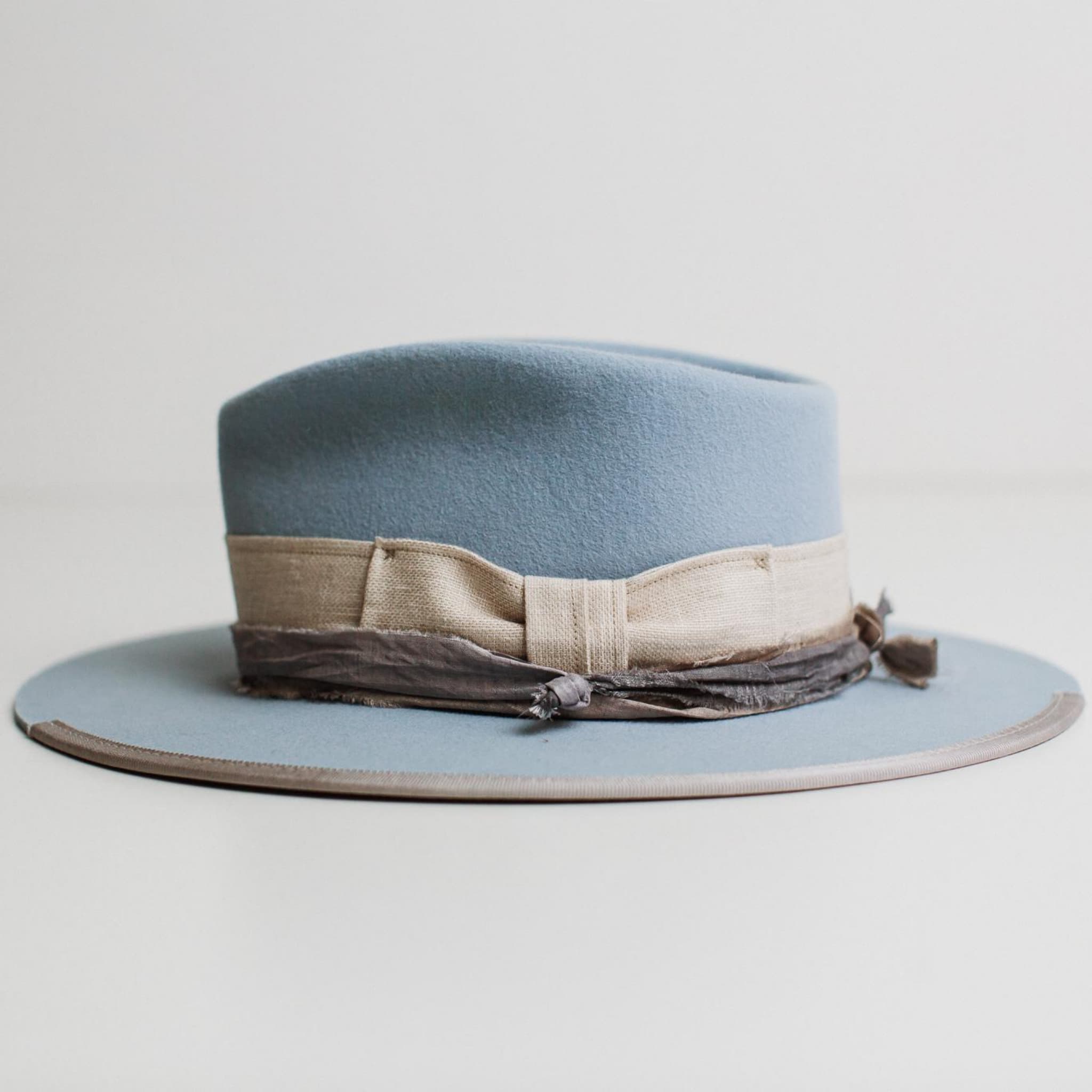 Left side view of Perfect Storm crystal blue felt hat by PHYLLi Designs showing linen band, stormy blue sari silk trim and silver grosgrain brim edge.