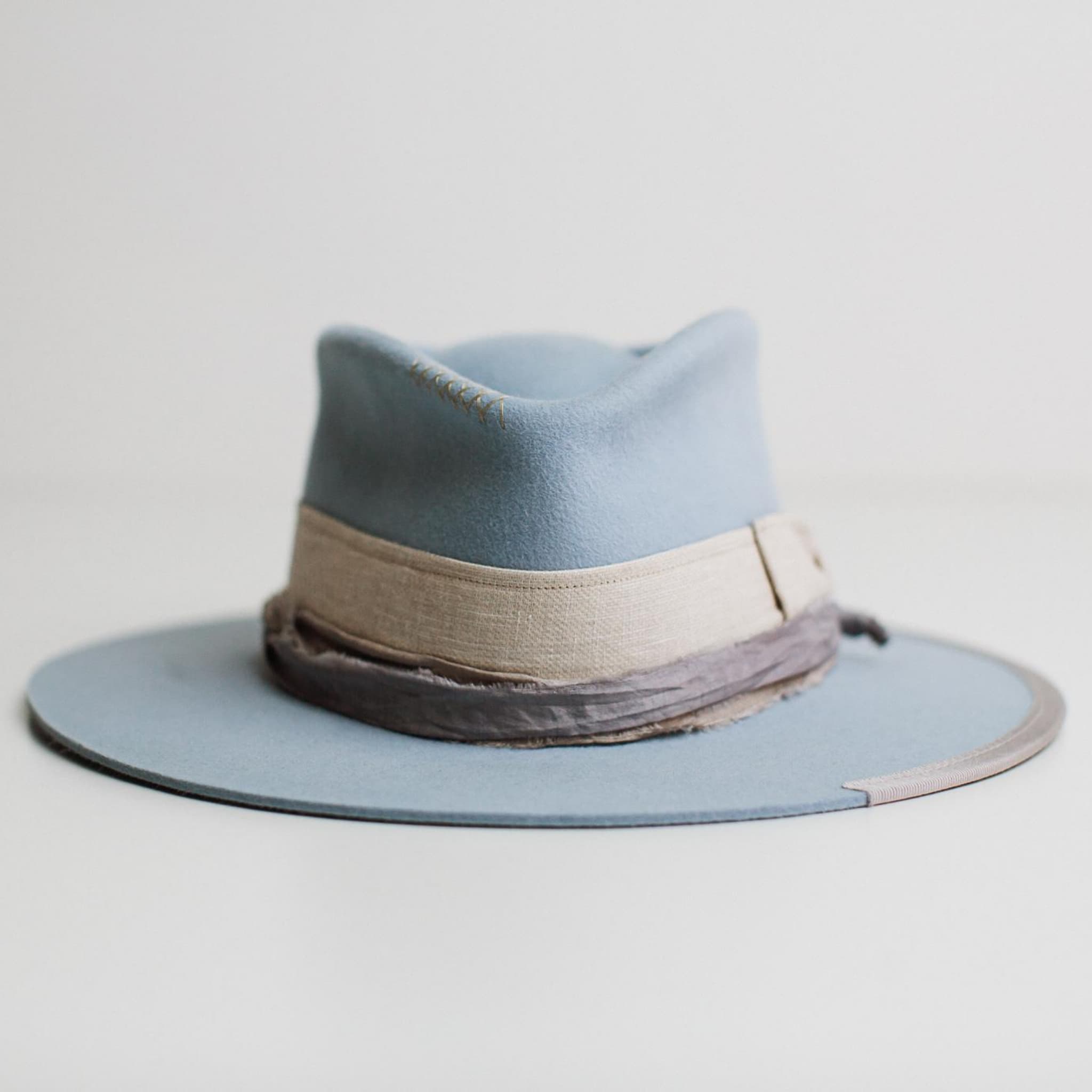 Front view of Perfect Storm crystal blue premium felt hat by PHYLLi Designs with natural linen bow band and stormy blue sari silk trim on white background.