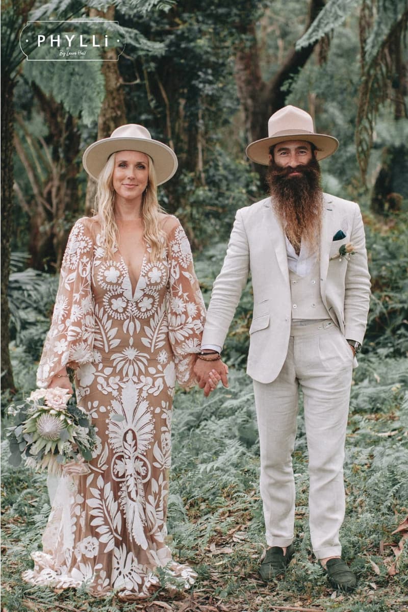 Bride and groom wearing neutral felt wedding hats by PHYLLi Designs standing in a lush forest setting for a bohemian wedding portrait.