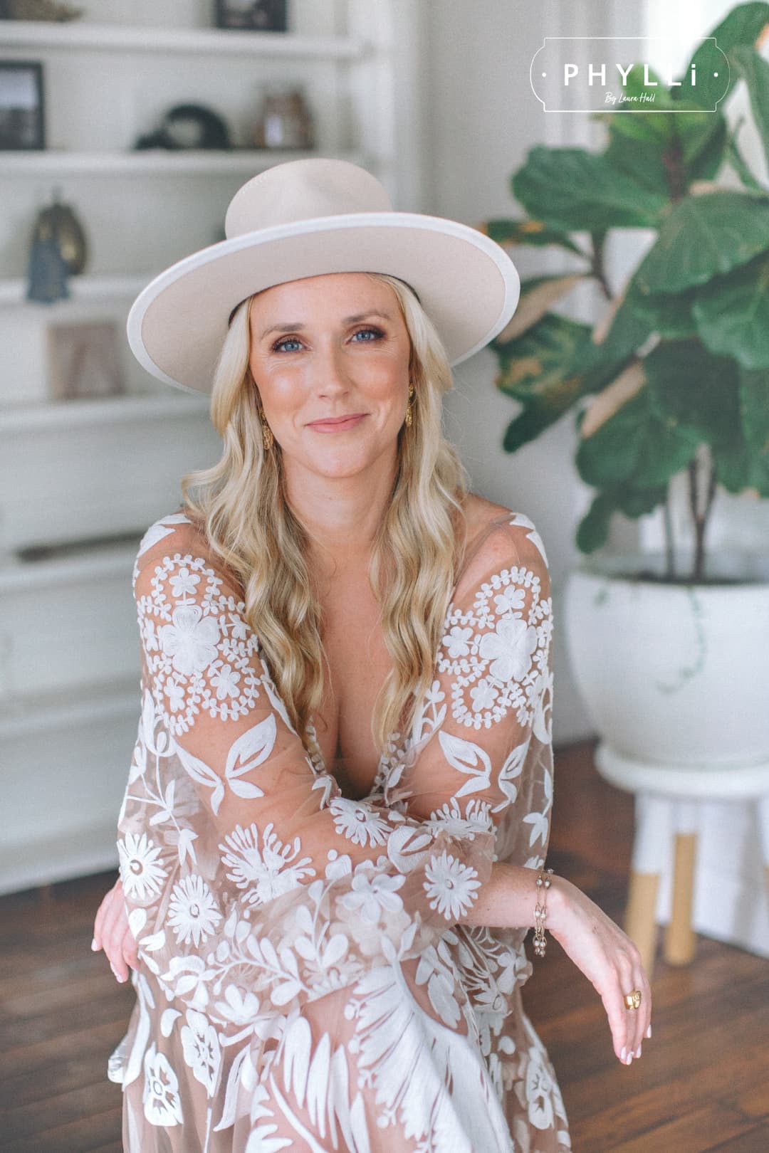 Bride wearing a cream felt wedding hat by PHYLLi Designs with embroidered bridal gown in a light-filled home interior.