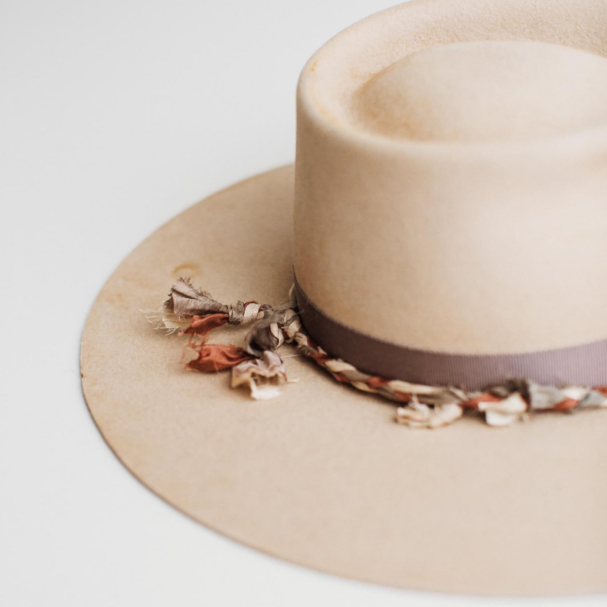 Close-up detail of Plum Twist beige felt hat by PHYLLi Designs showing hand-stitched crosses and plaited sari silk trim in mauve, ivory and plum.