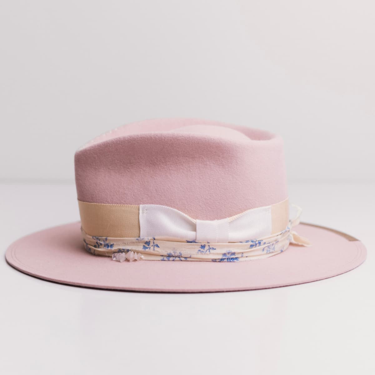 Left side view of the Posie Baby Pink felt hat by PHYLLi Designs with taupe grosgrain brim trim and cream-blue sari silk trim.