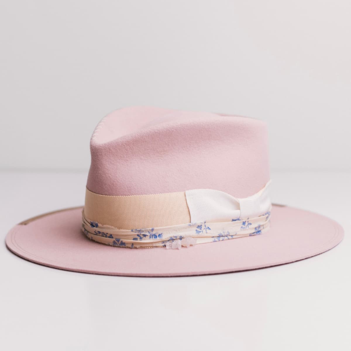 Front left angle of the Posie Baby Pink felt hat by PHYLLi Designs with rose quartz crystal cluster and cream and blue patterned sari silk trimming.