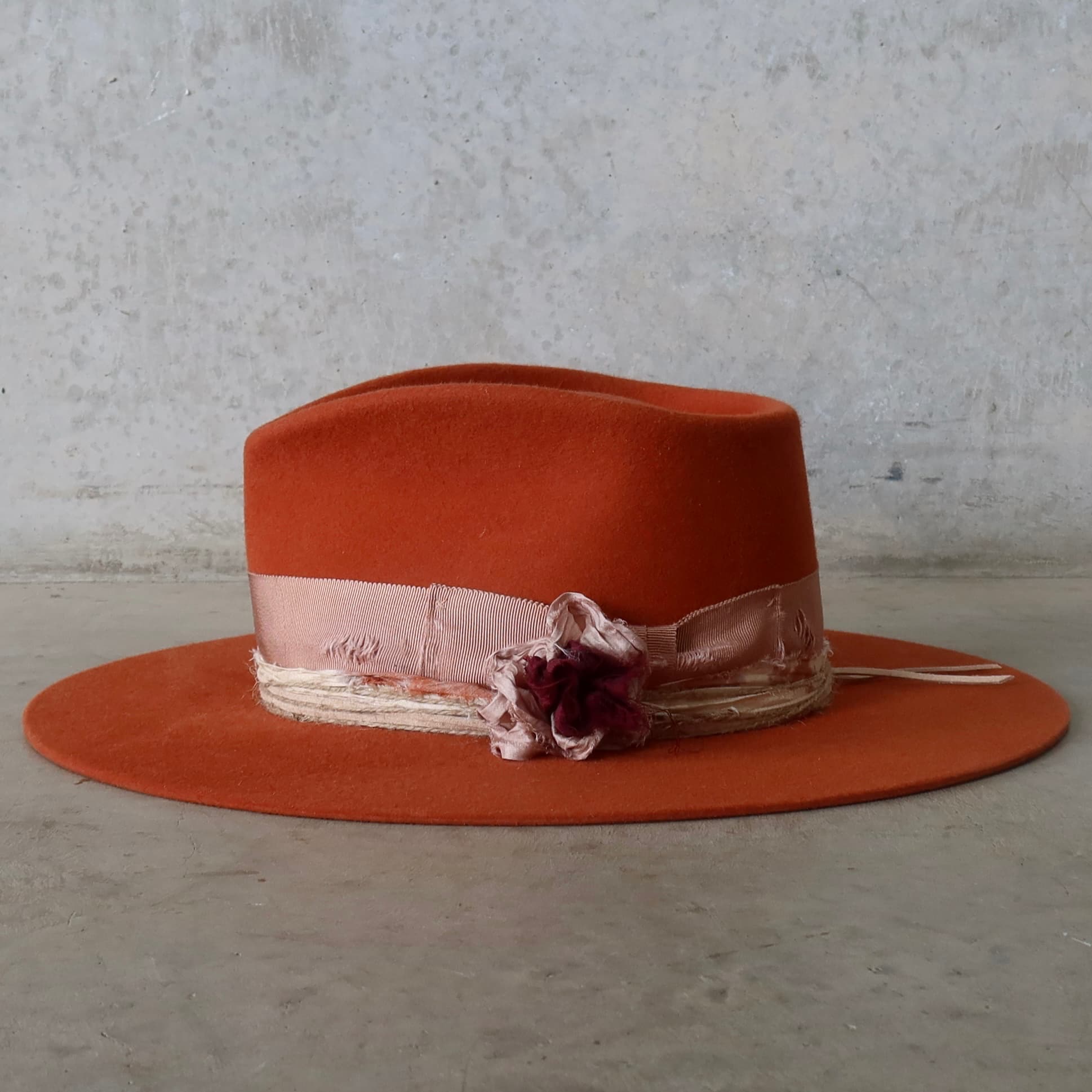Left side view of the spiced pumpkin felt hat Pumpkin Bloom by PHYLLi Designs with sari silk lapel blooms and twine wraps.