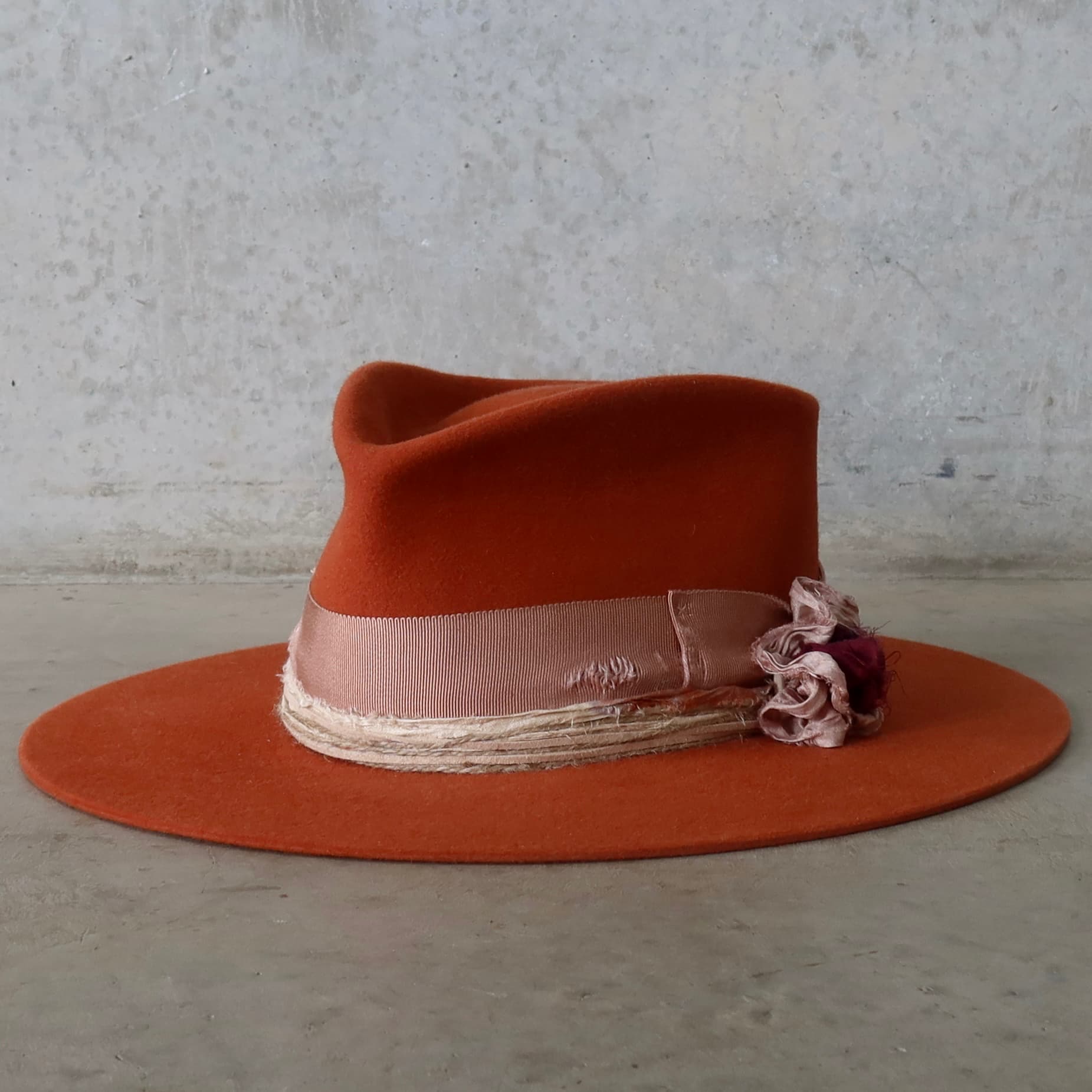 Front left angle of the spiced pumpkin felt hat Pumpkin Bloom by PHYLLi Designs with dirty rose grosgrain bow band, twine wraps and sari silk lapel bloom.