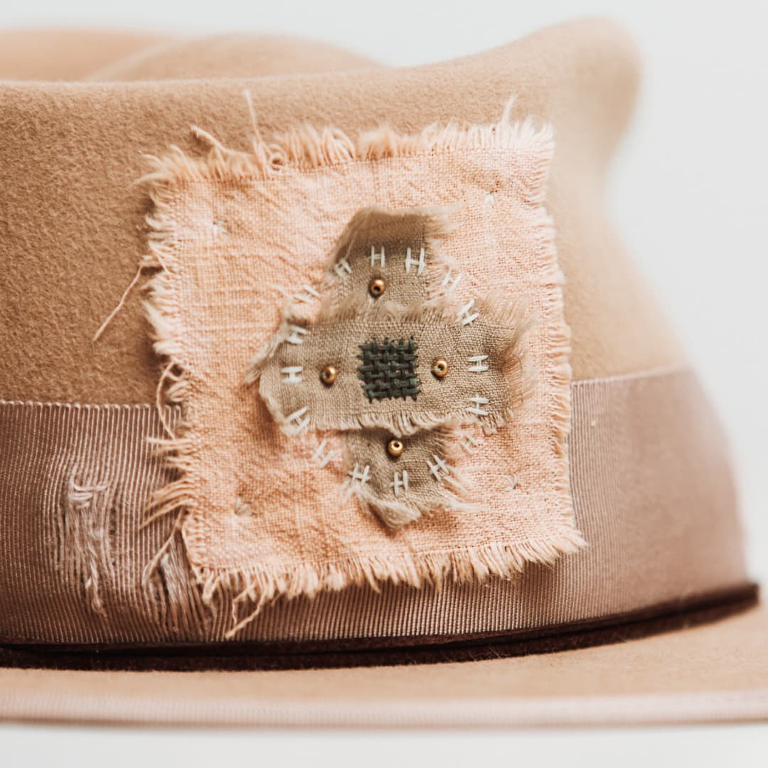 Close up detail of the Reiko felt hat showing pink linen cross patterned patch with ivory and grey stitching and gold beading.