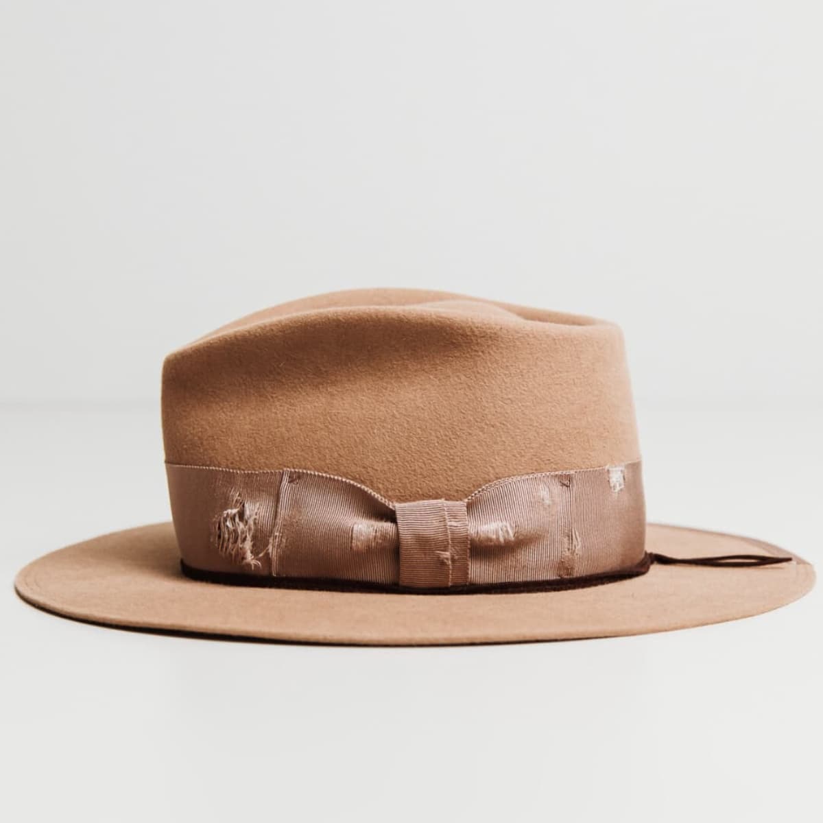 Left side view of the Reiko camel felt hat by PHYLLi Designs with distressed plaster grosgrain band and suede string trim.