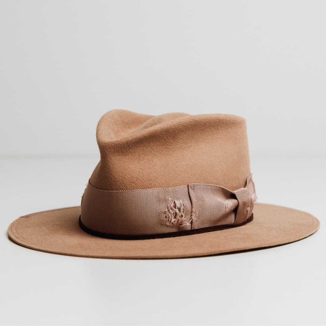 Front left angle of the Reiko camel felt hat by PHYLLi Designs with distressed plaster grosgrain band and suede wraps.