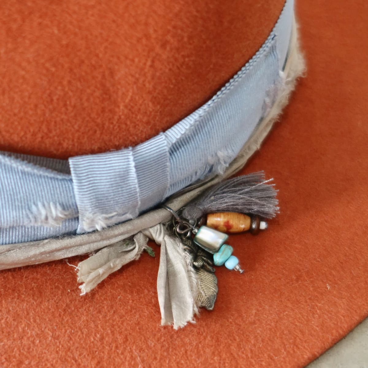 Close up detail of the Road Less Travelled felt hat showing charm cluster with navy tassel, silver feather charm and bead cluster.