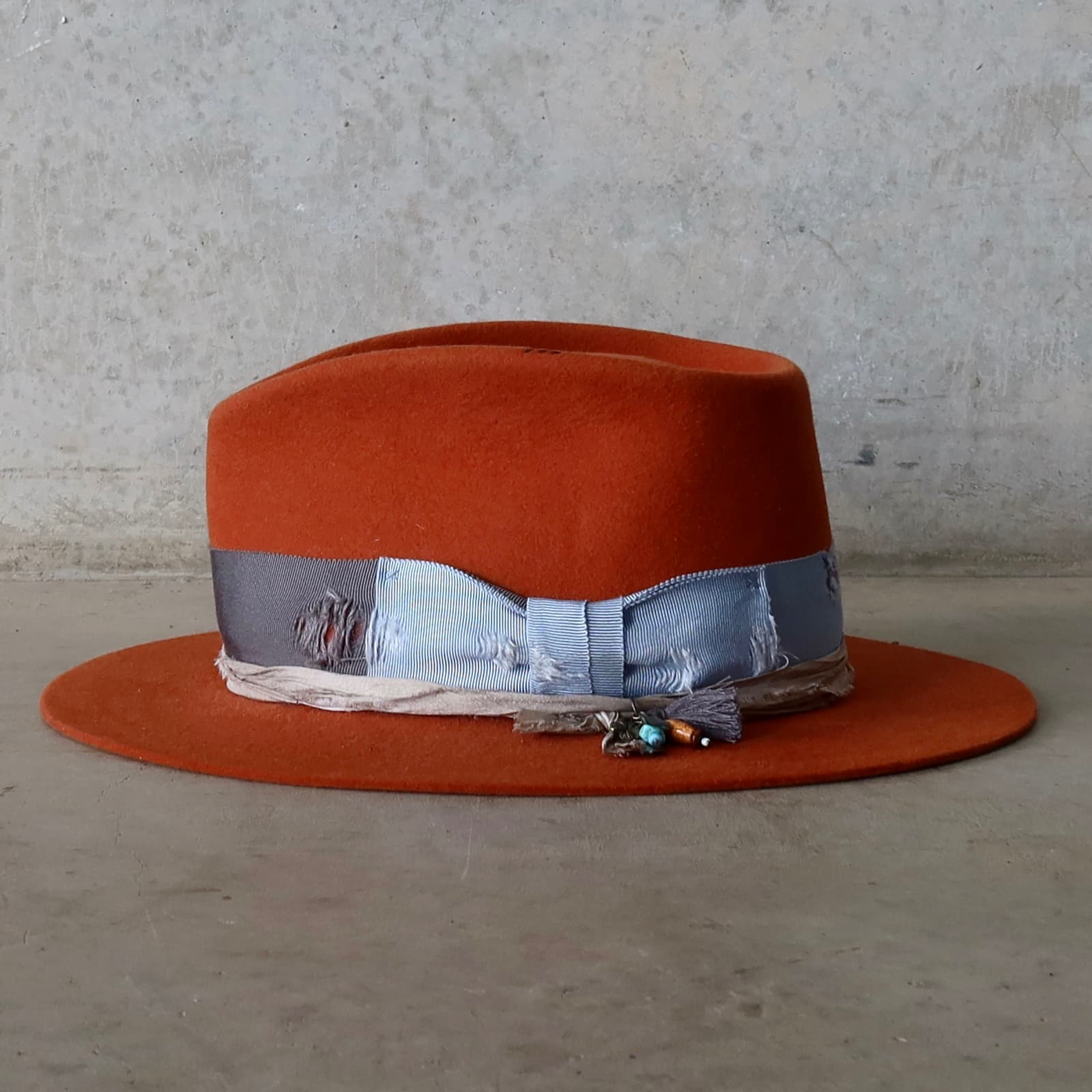 Left side view of the Road Less Travelled spiced pumpkin felt hat by PHYLLi Designs with charm cluster featuring navy tassel, silver charm and bead details.