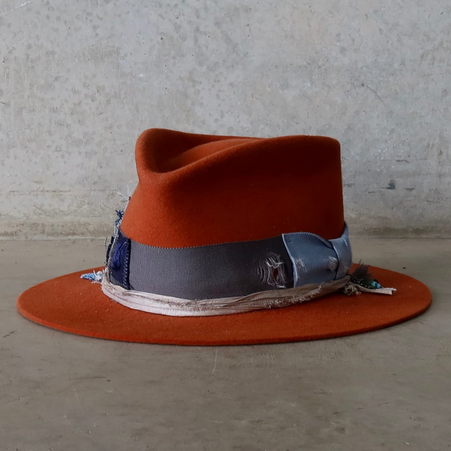 Front left angle of the Road Less Travelled spiced pumpkin felt hat by PHYLLi Designs with distressed grosgrain bow band and sari silk trim in Smoke.
