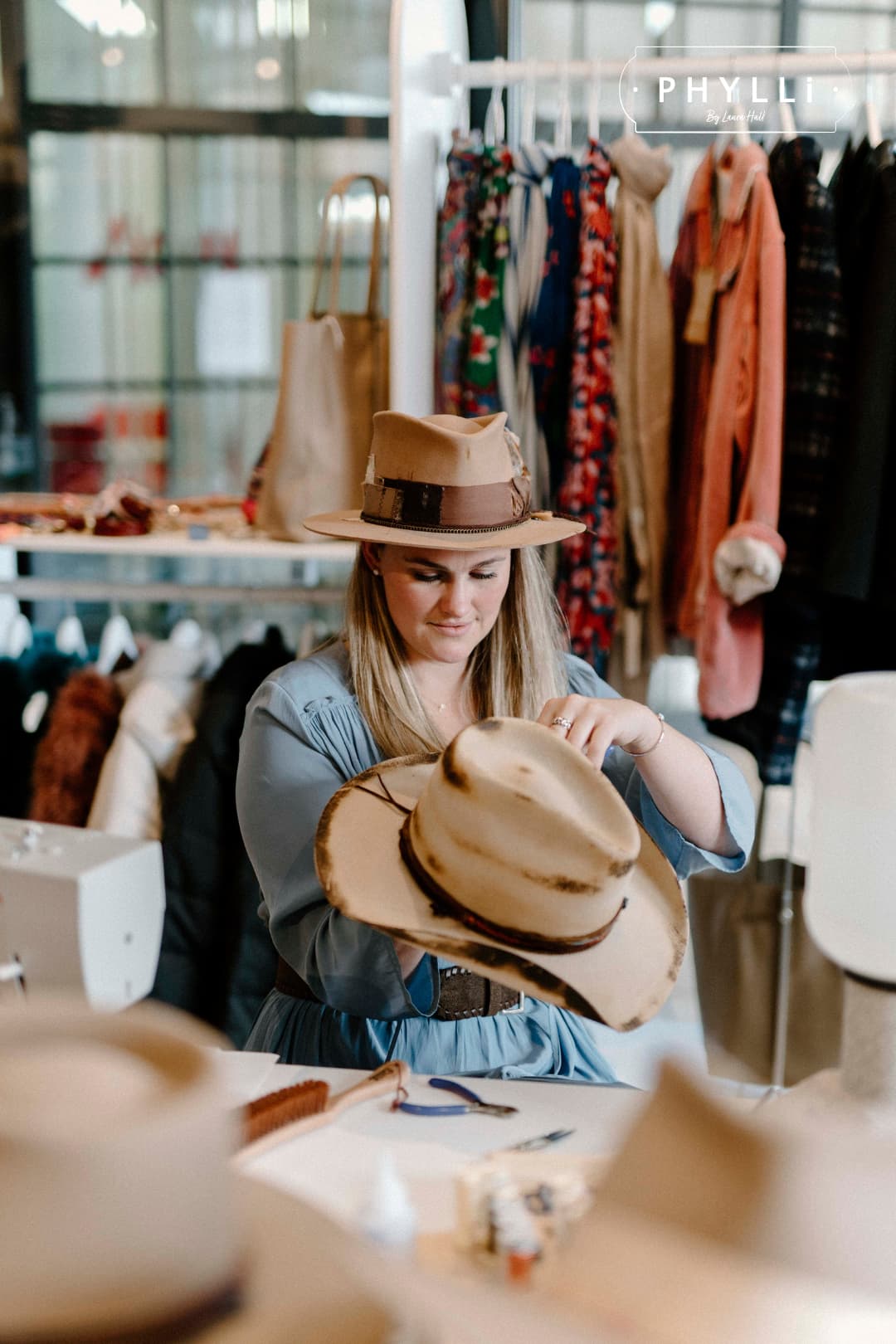 Laura Hall trimming a felt hat in the PHYLLi Designs studio while wearing the Roadie camel hat.