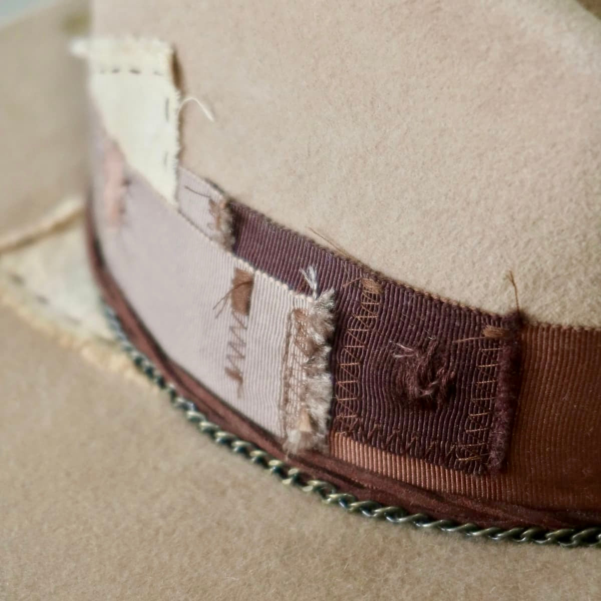 Close up of Roadie felt hat by PHYLLi Designs showing distressed grosgrain patches and bronze crown chain.