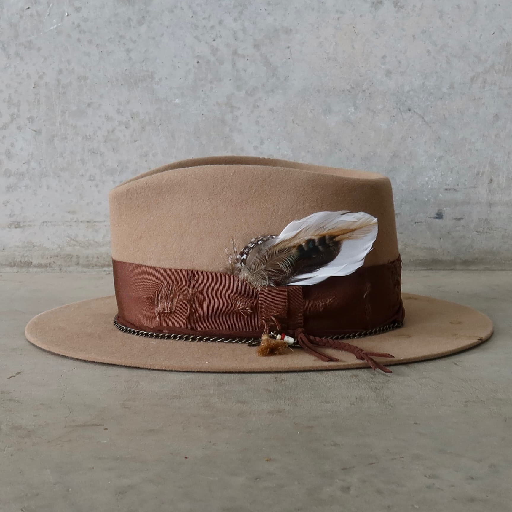 Left side view of Roadie felt hat by PHYLLi Designs with feather bunch and charm cluster featuring tassel and bronze pendant charms.