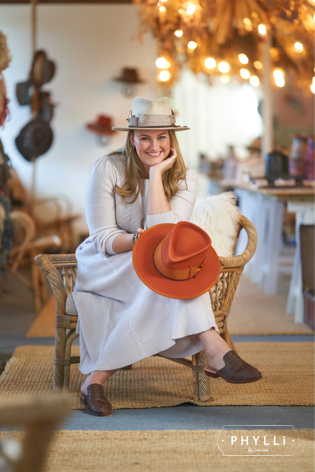 PHYLLi founder Laura Hall wearing the Roadie beige felt hat by PHYLLi Designs with feather cluster and suede tie trim in a hat studio.