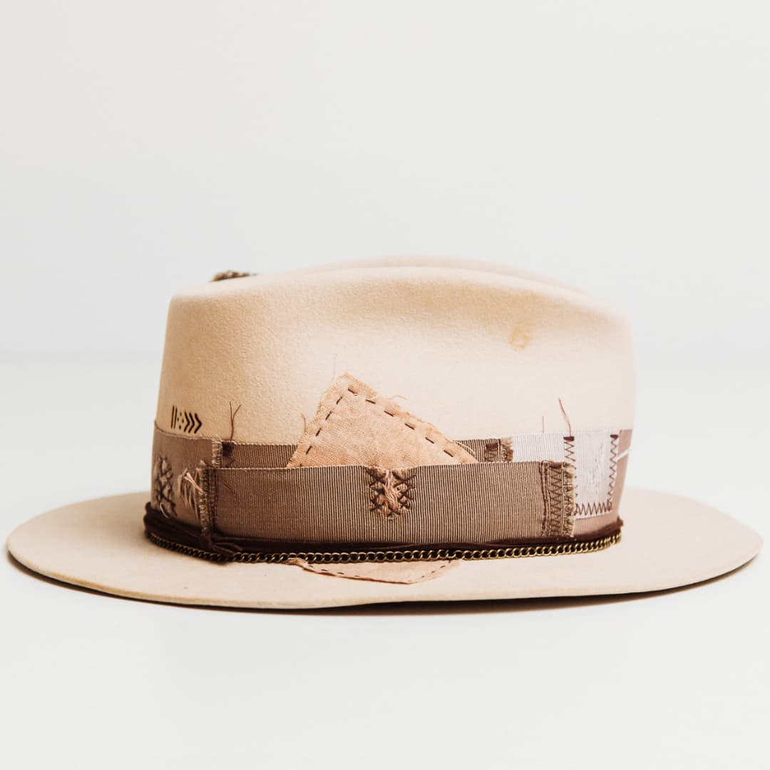 Right side view of the Roadie beige felt hat by PHYLLi Designs with distressed plaster grosgrain band, patchwork fabric panels and brass chain brim trim.