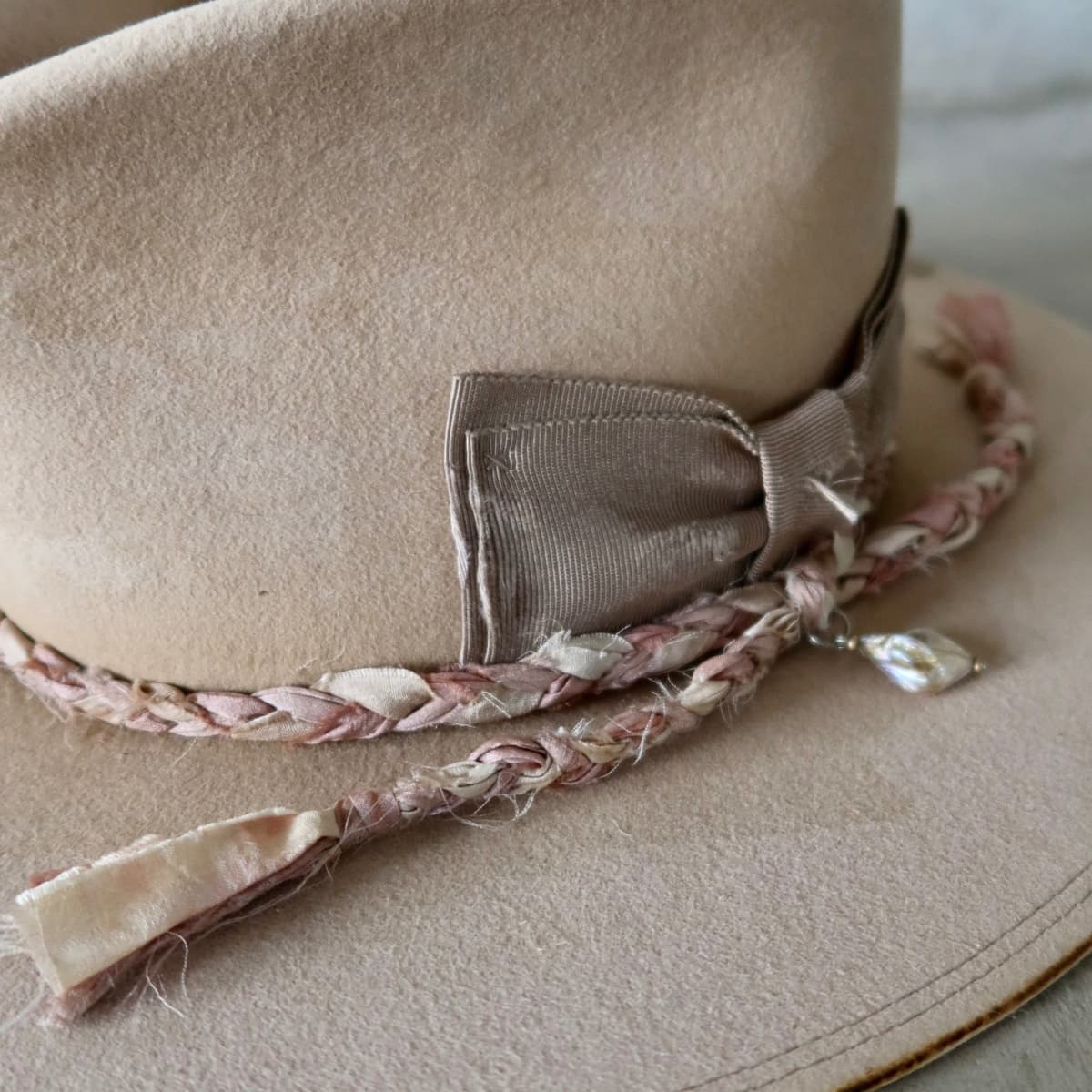 Close up detail of the Ryoan Limited Edition felt hat showing taupe Japanese grosgrain floating double bow with plaited sari silk trimming in tonal pinks and rough pearl pendant.