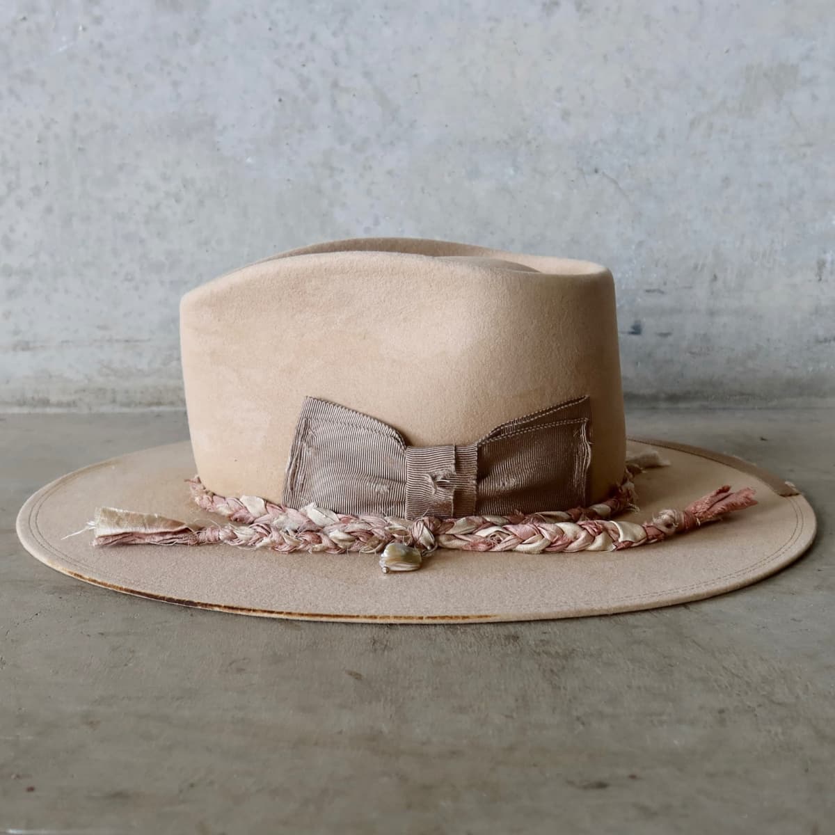 Left side view of the sand distressed felt hat Ryoan Limited Edition by PHYLLi Designs with plaited sari silk trimmings and rough pearl pendant.