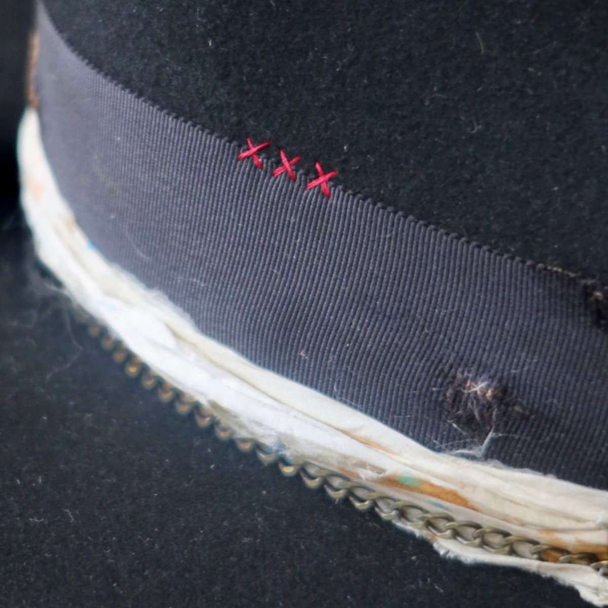 Close up detail of the Saint felt hat showing burgundy hand-stitched crosses on the side crown.