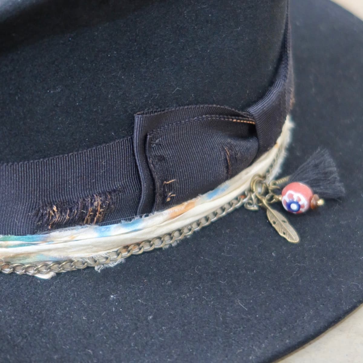 Close up detail of the Saint felt hat showing distressed black Japanese grosgrain bow band and bronze crown chain.