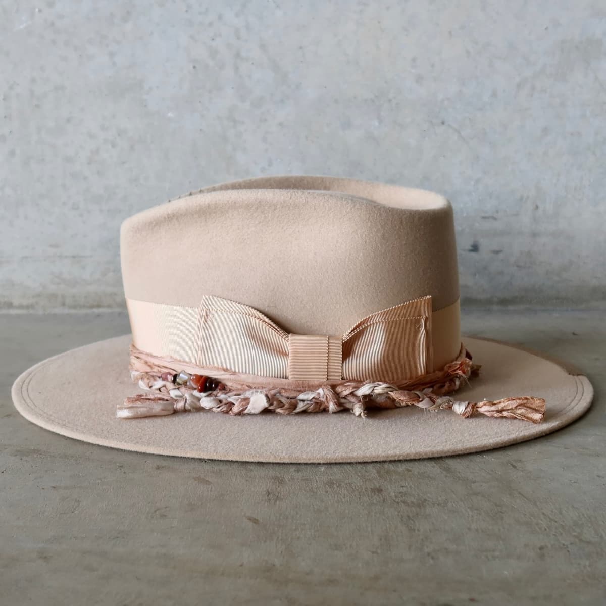 Left side view of the sand felt hat Sandstone Limited Edition by PHYLLi Designs with plaited sari silk trimmings in tonal colours and crystal cluster.