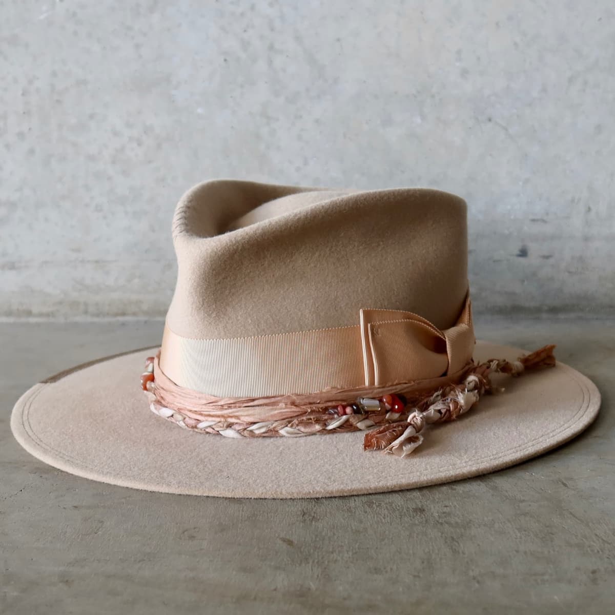 Front left angle of the sand felt hat Sandstone Limited Edition by PHYLLi Designs with apricot Japanese grosgrain double bow band and plaited sari silk trimmings in tonal colours.