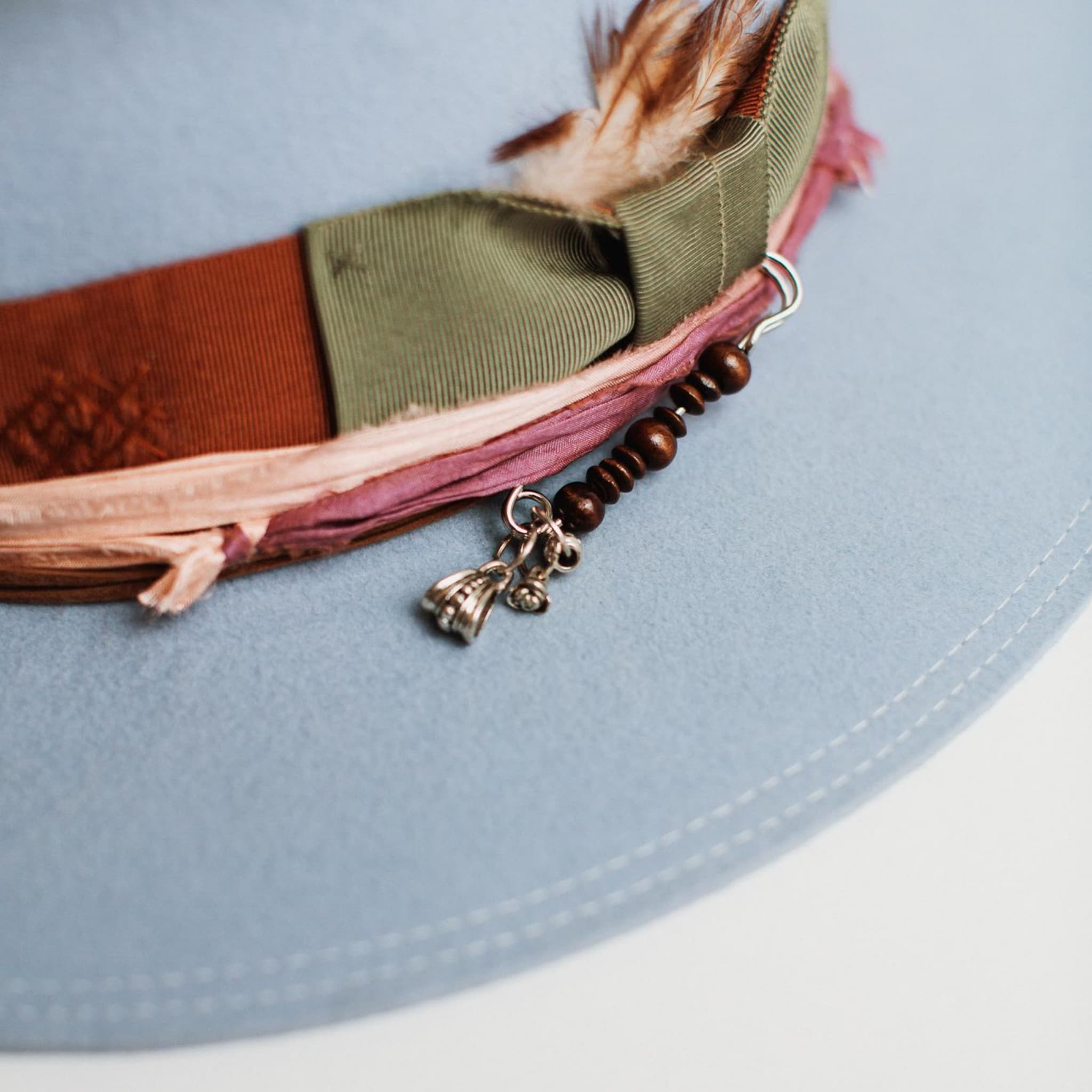 Close-up detail of Santa Monica crystal blue felt hat by PHYLLi Designs showing rust band, sari silk trim and silver hat pin.