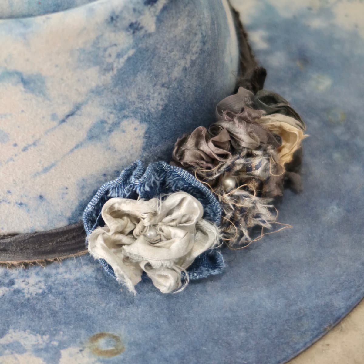 Close up detail of the Shibori Limited Edition felt hat showing sari silk lapel blooms in indigo denim and pearl centre.