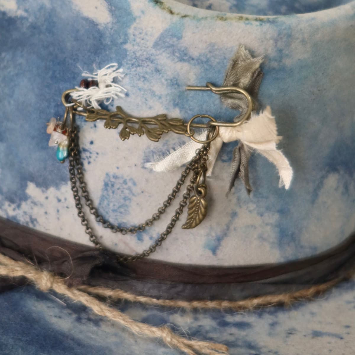 Close up detail of the Shibori Limited Edition felt hat showing bronze hat pin with chains and quartz crystal charms.