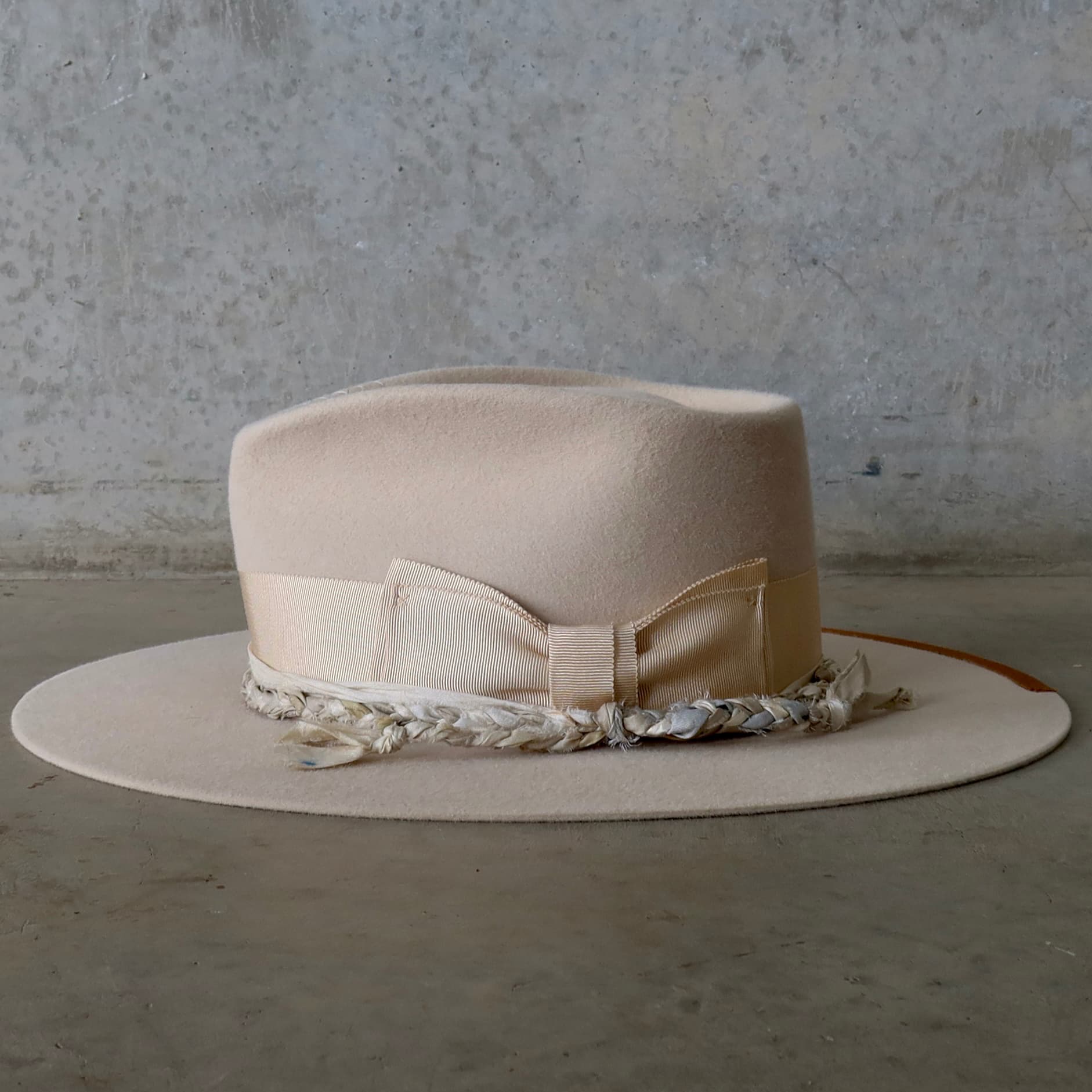Left side view of the beige felt hat Shoalhaven by PHYLLi Designs with sand grosgrain band and plaited sari silk trimming.