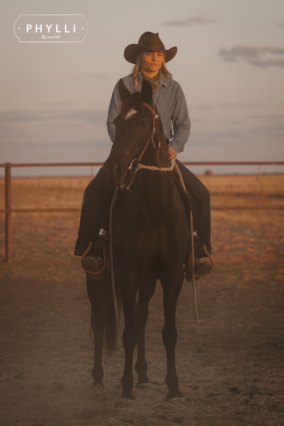 Woman riding a horse wearing the chocolate cowboy hat Spicer by PHYLLi Designs with chocolate grosgrain band in a rural paddock at sunset.