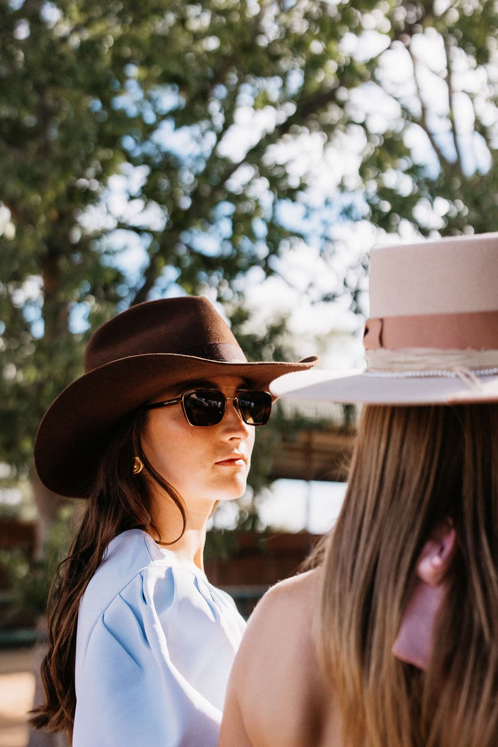 Close up side profile of a woman wearing the PHYLLi Spicer chocolate cowboy felt hat and sunglasses outside among trees.