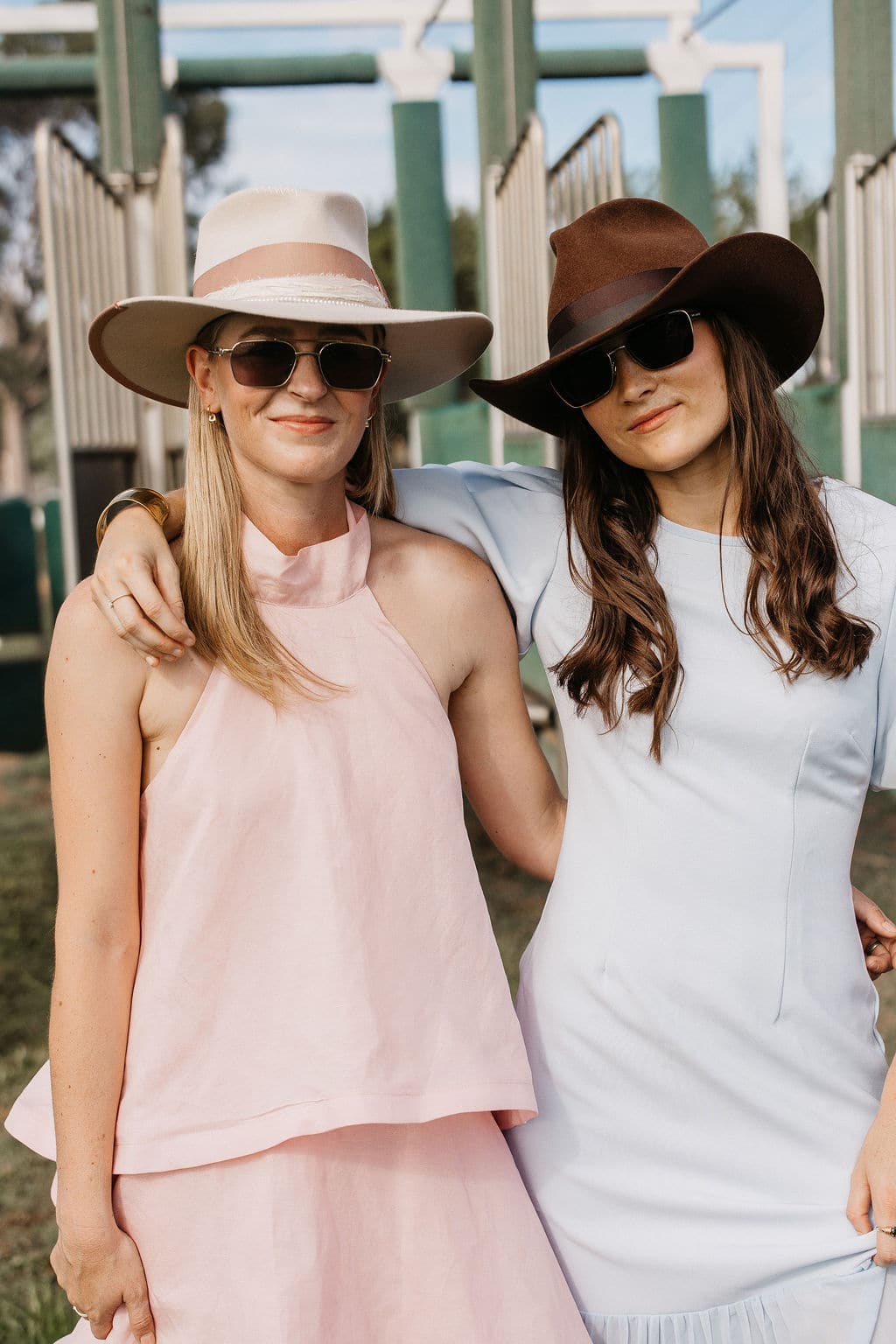 Woman wearing the PHYLLi Spicer chocolate felt hat and sunglasses standing close with a friend outdoors by the stalls.