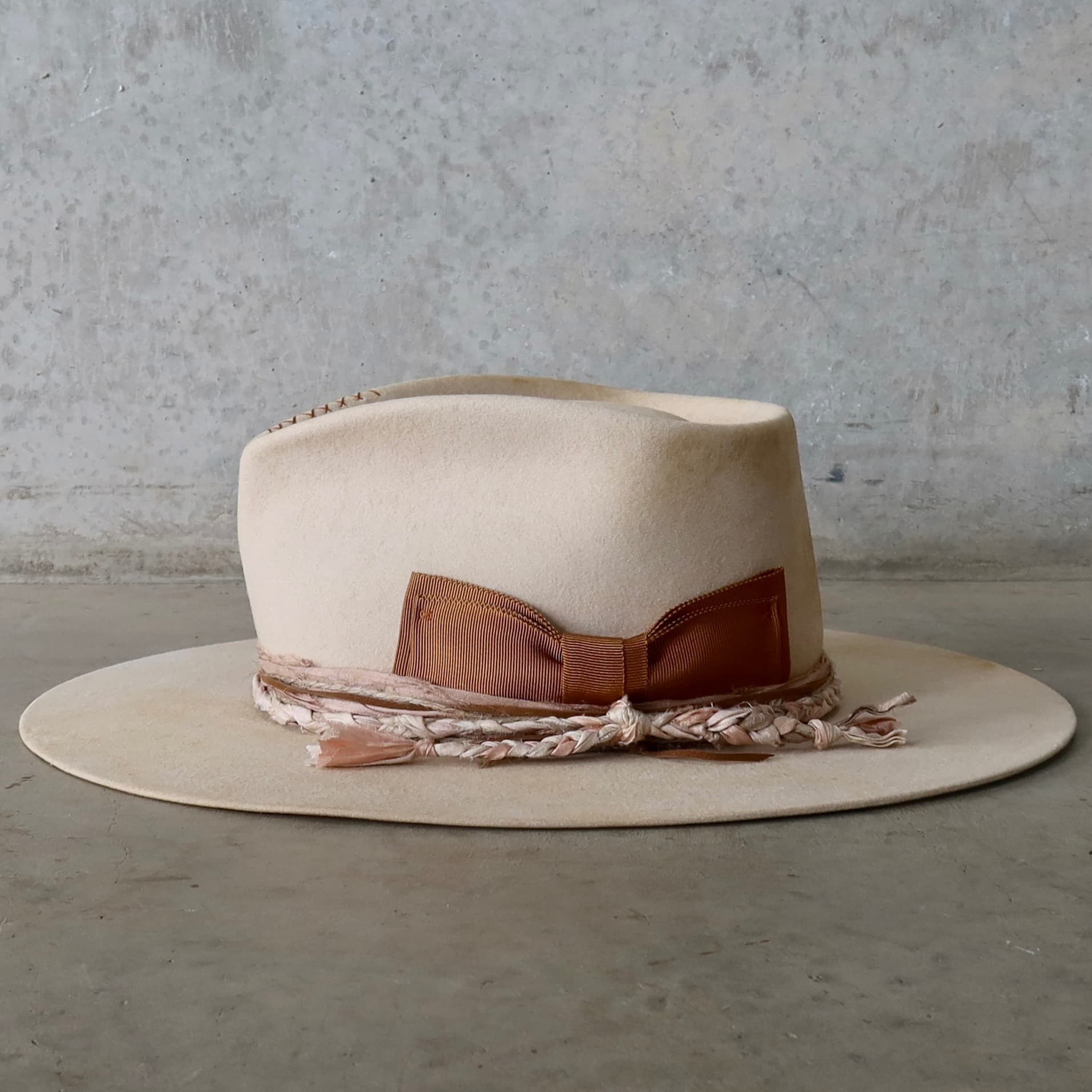 Left side view of the beige distressed felt hat Starlight by PHYLLi Designs with copper grosgrain floating bow and plaited sari silk trim.
