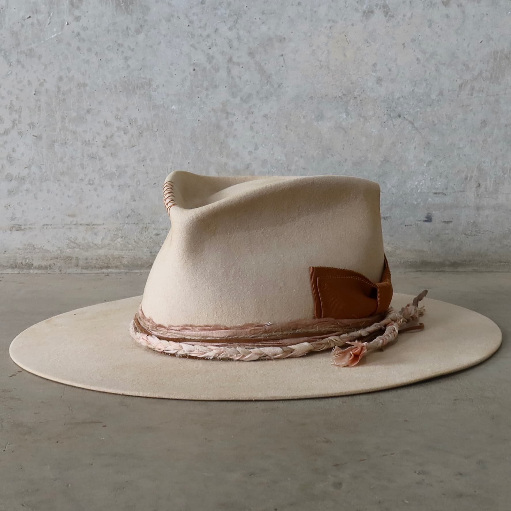 Front left angle of the beige distressed felt hat Starlight by PHYLLi Designs with copper grosgrain floating bow and dirty rose sari silk trim.
