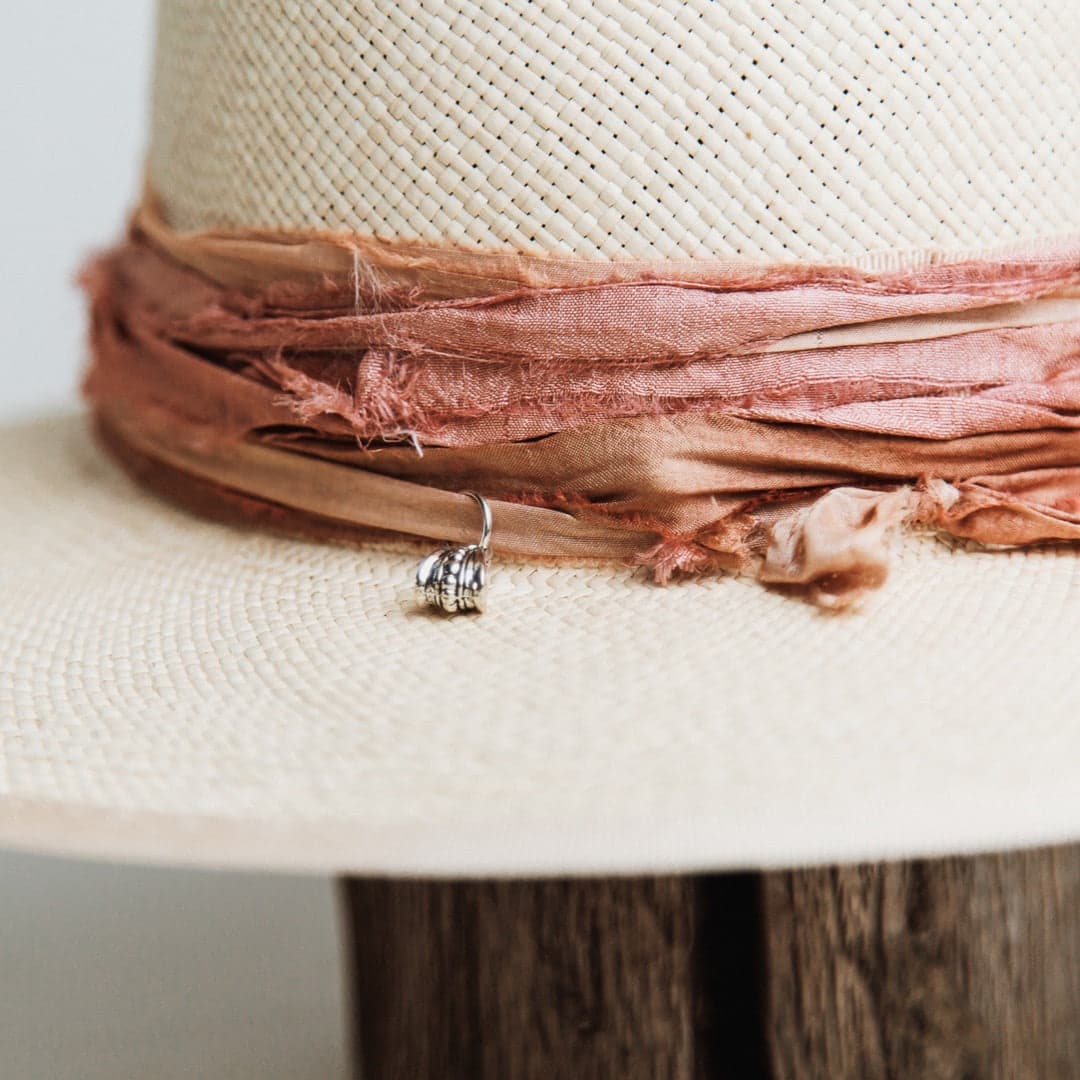 Close up detail of the Sunset Panama hat showing apricot sari silk trimming and silver pendant charm.