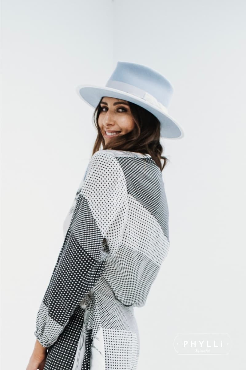 Woman wearing The Arrow crystal blue felt hat by PHYLLi Designs with ivory grosgrain brim trim and silver pendant charm.