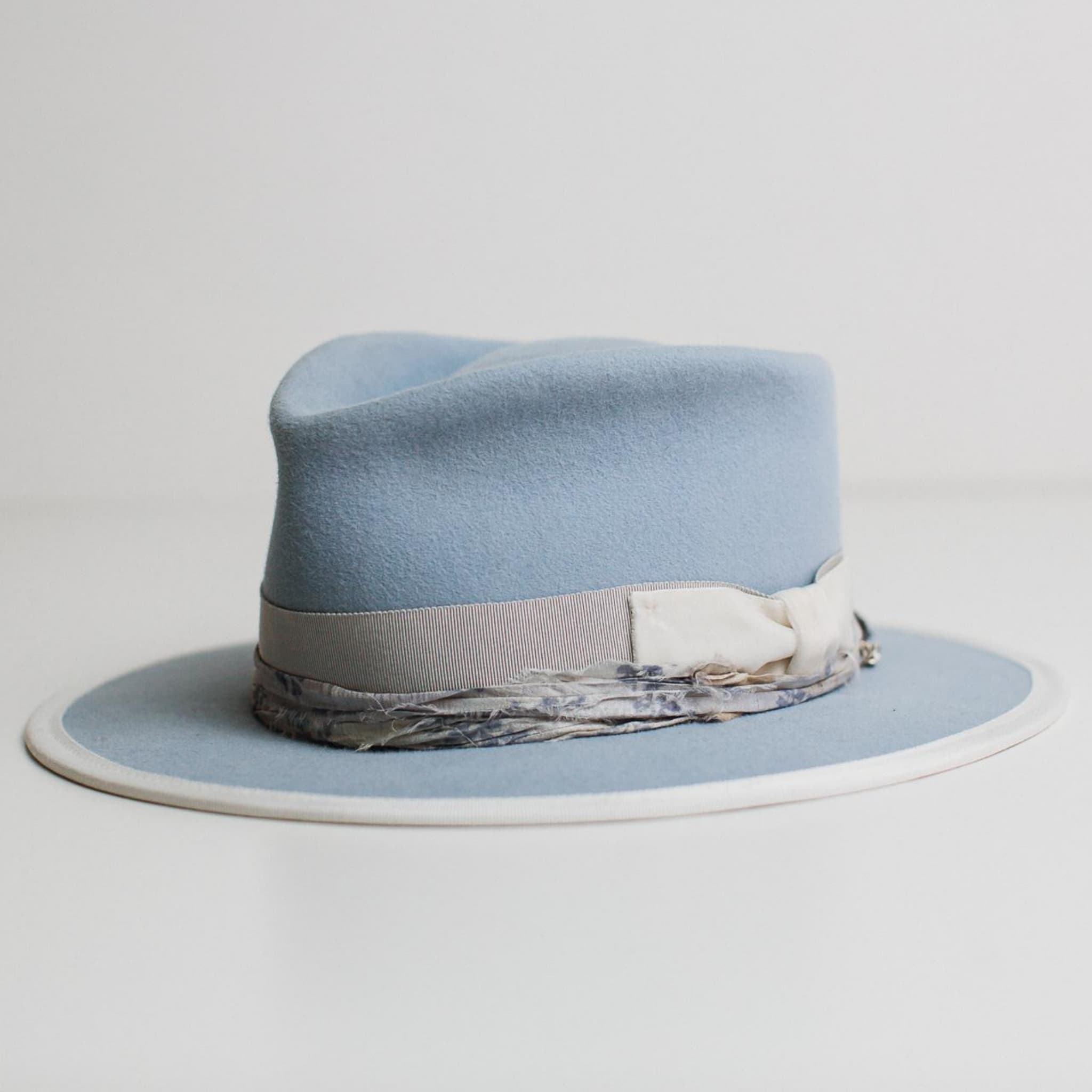 Front left angle of The Arrow crystal blue felt hat by PHYLLi Designs with dove Japanese grosgrain band, ivory velvet bow and dusty blue sari silk trim.