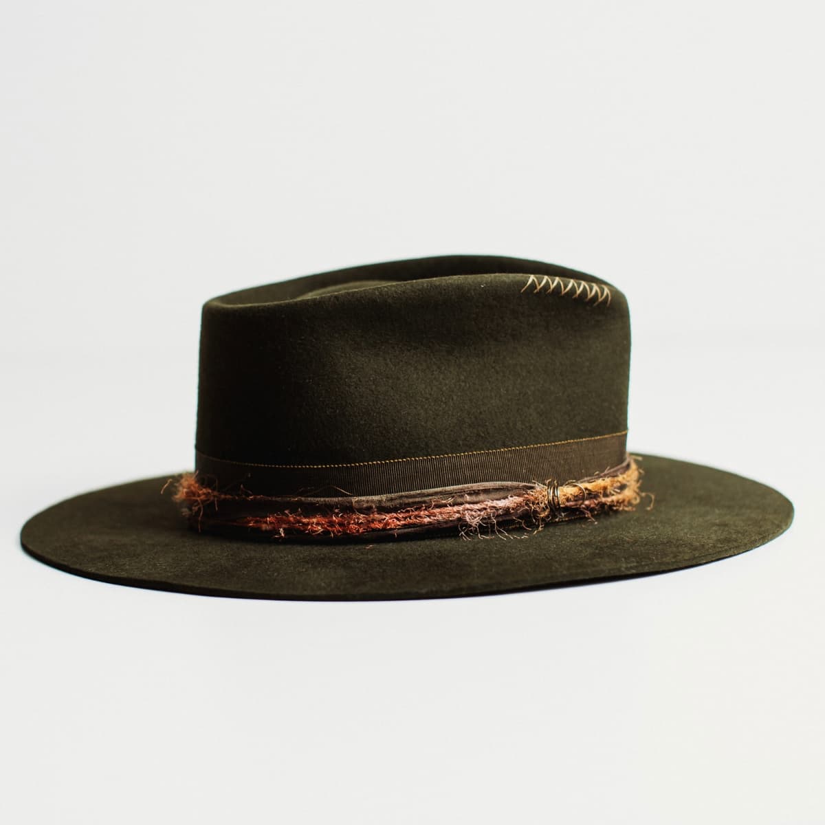 Right side view of dark olive felt hat with distressed layered band on a light grey background.