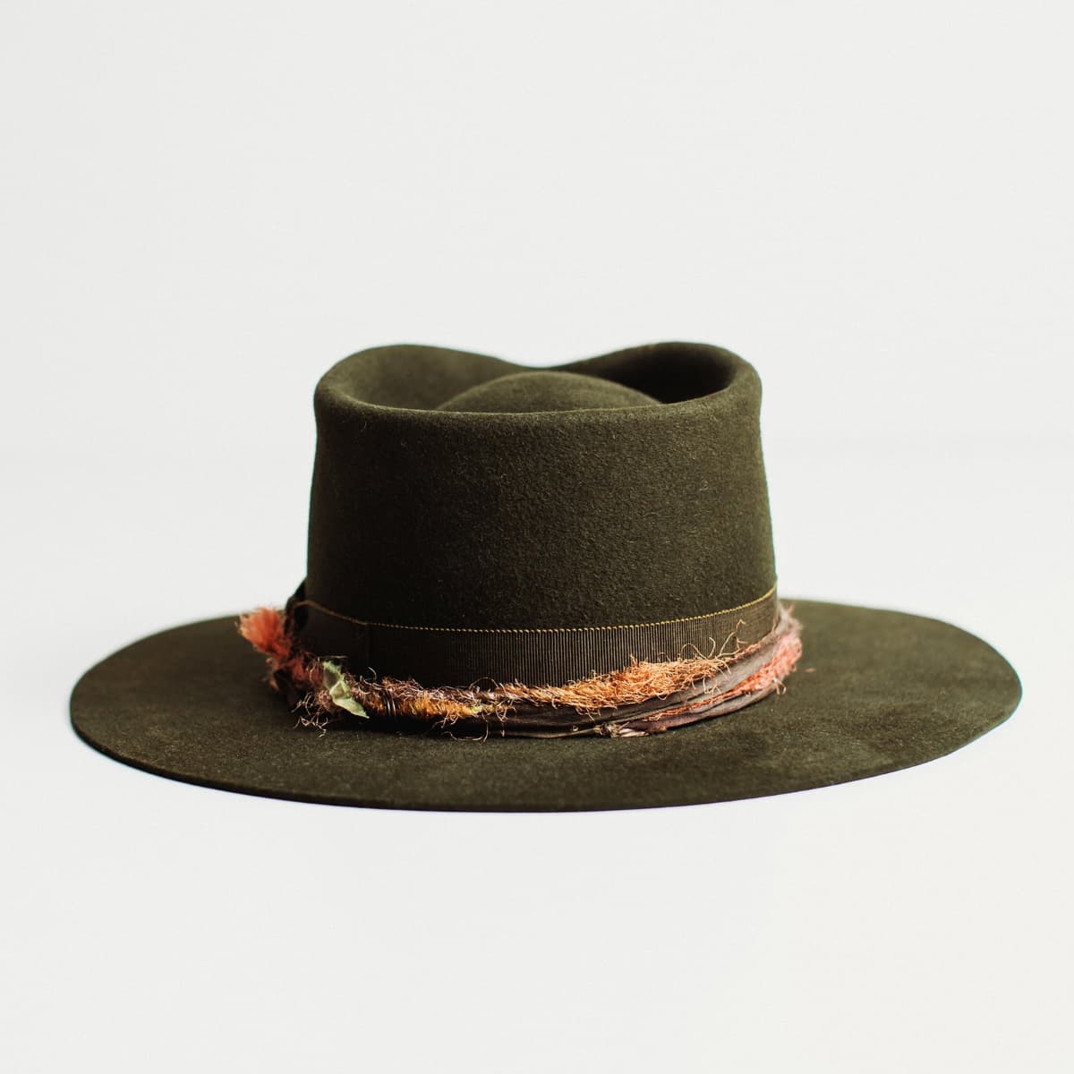 Back view of dark olive felt hat with distressed layered band on a light grey background.