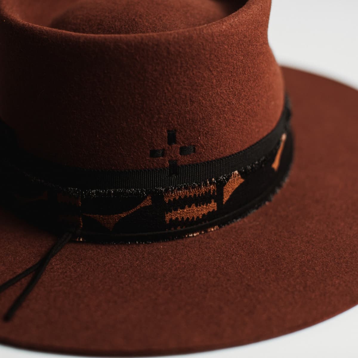 Close-up detail of russet felt hat showing decorative band and felt texture.