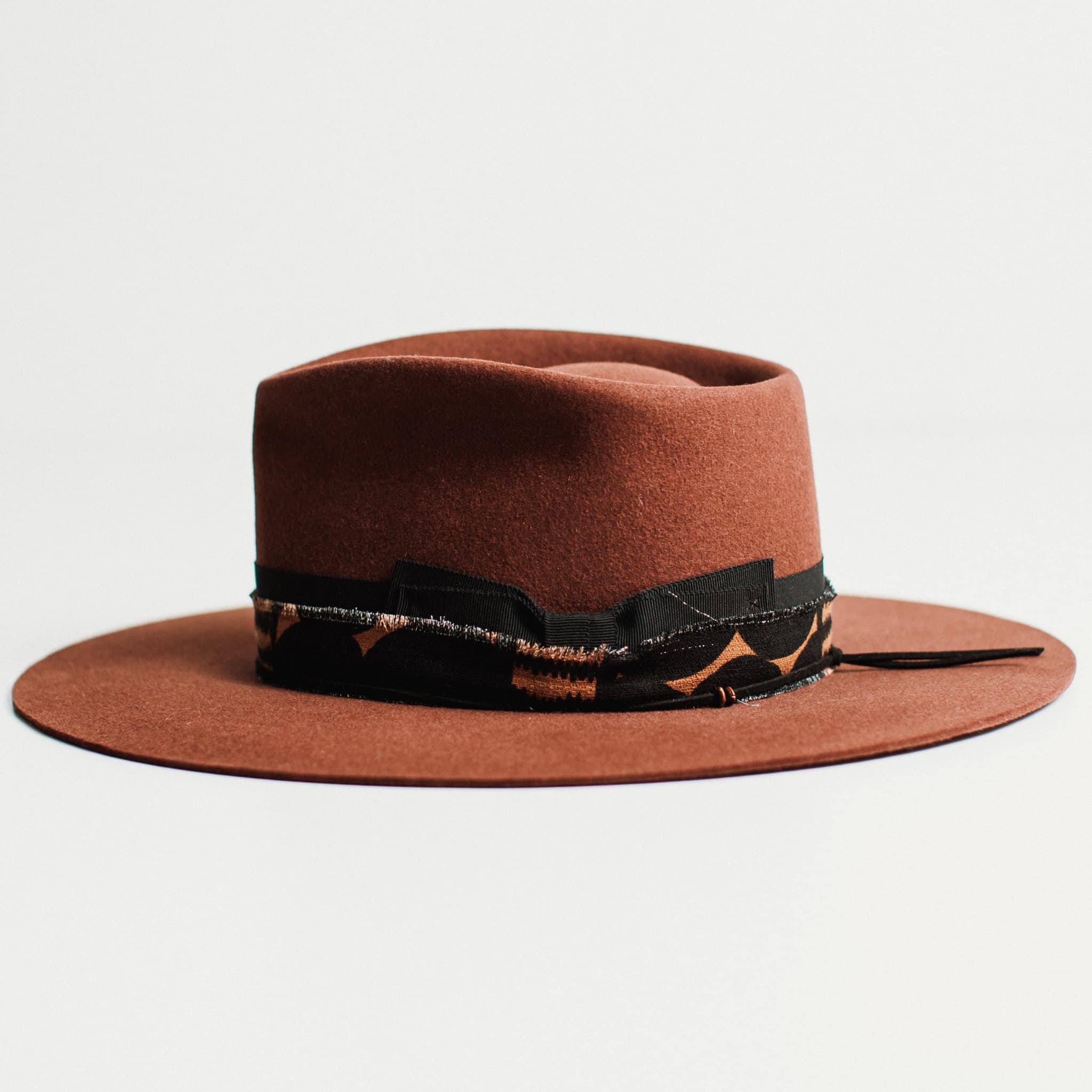 Side view of russet felt hat with decorative band by PHYLLi Designs on a light grey background.