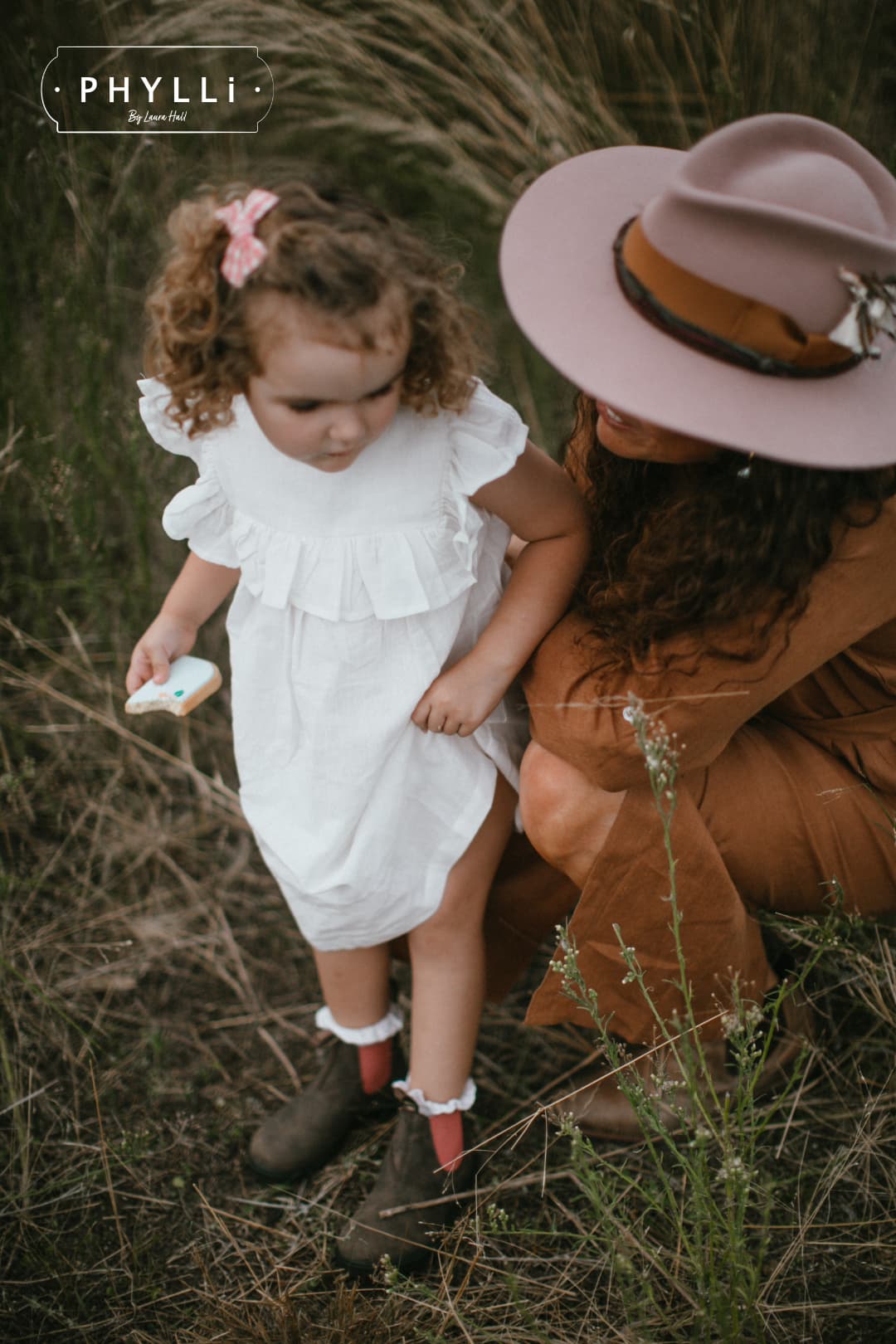 Woman wearing The Blush felt hat crouching beside child in grassy field.