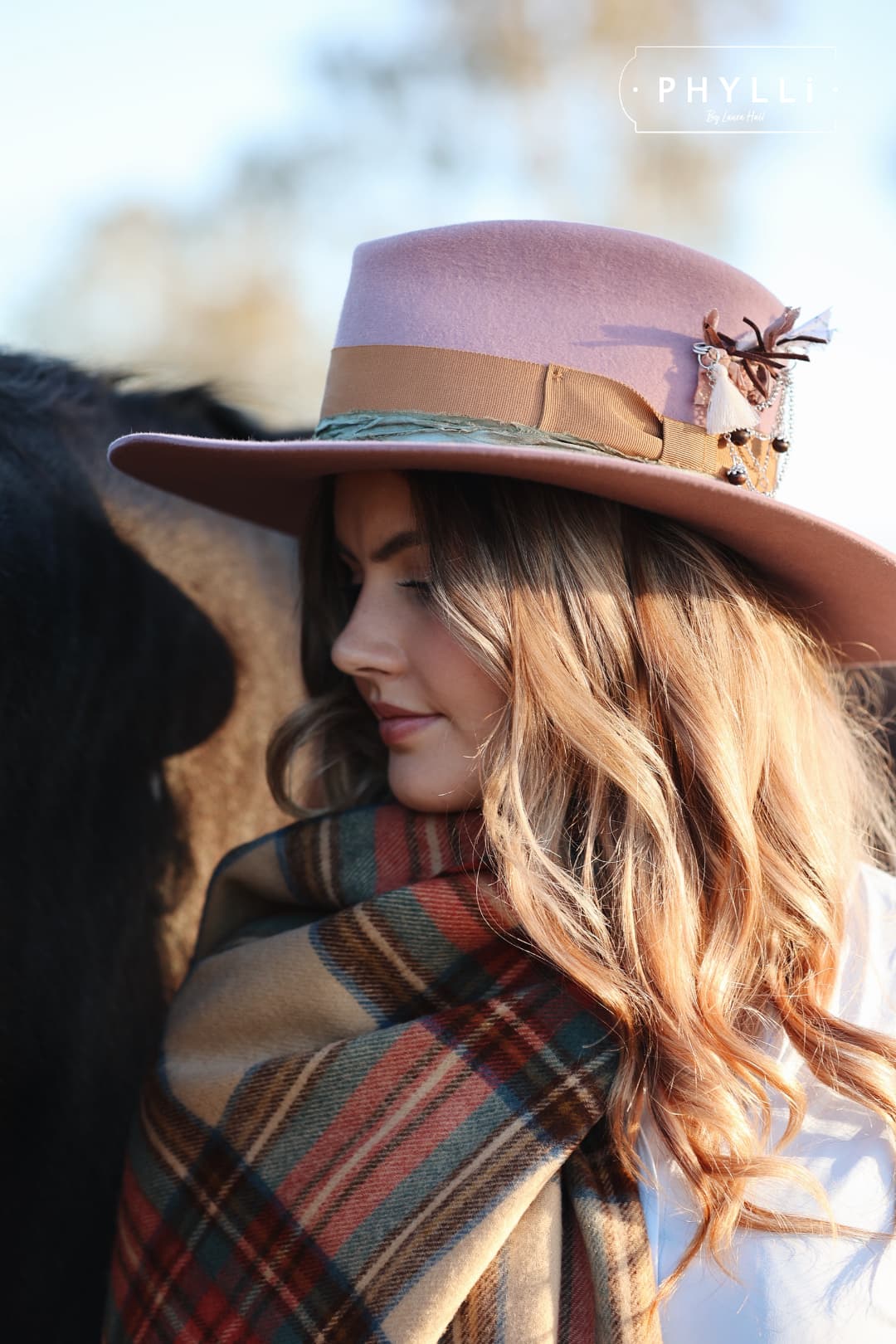Side profile of woman wearing The Blush pink felt hat with copper band beside horse.