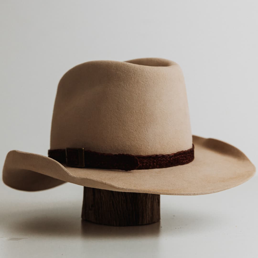 Back left angle of The Contractor premium felt hat in Beige with 12 strand plaited leather hat band in Chocolate featuring bronze buckle.