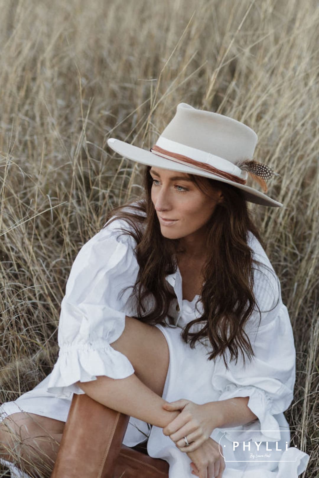 Woman wearing The Dartbrook beige felt hat by PHYLLi Designs sitting in dry grass.
