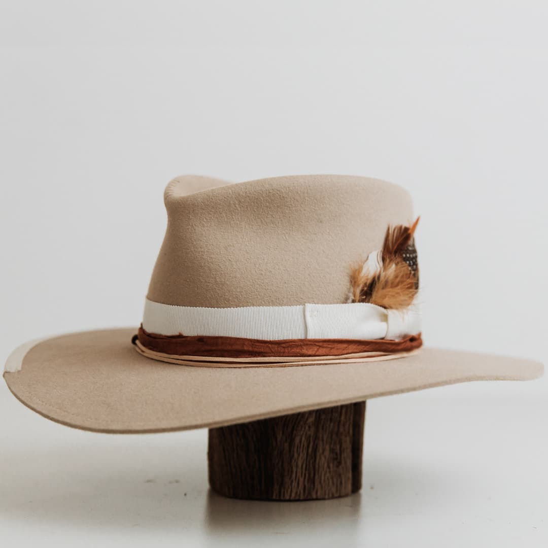 Front left angle of The Dartbrook beige felt hat featuring ivory grosgrain bow band and feather detail.